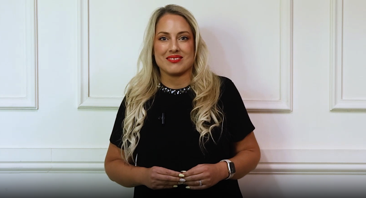 Smiling woman standing against white wall wearing black dress.