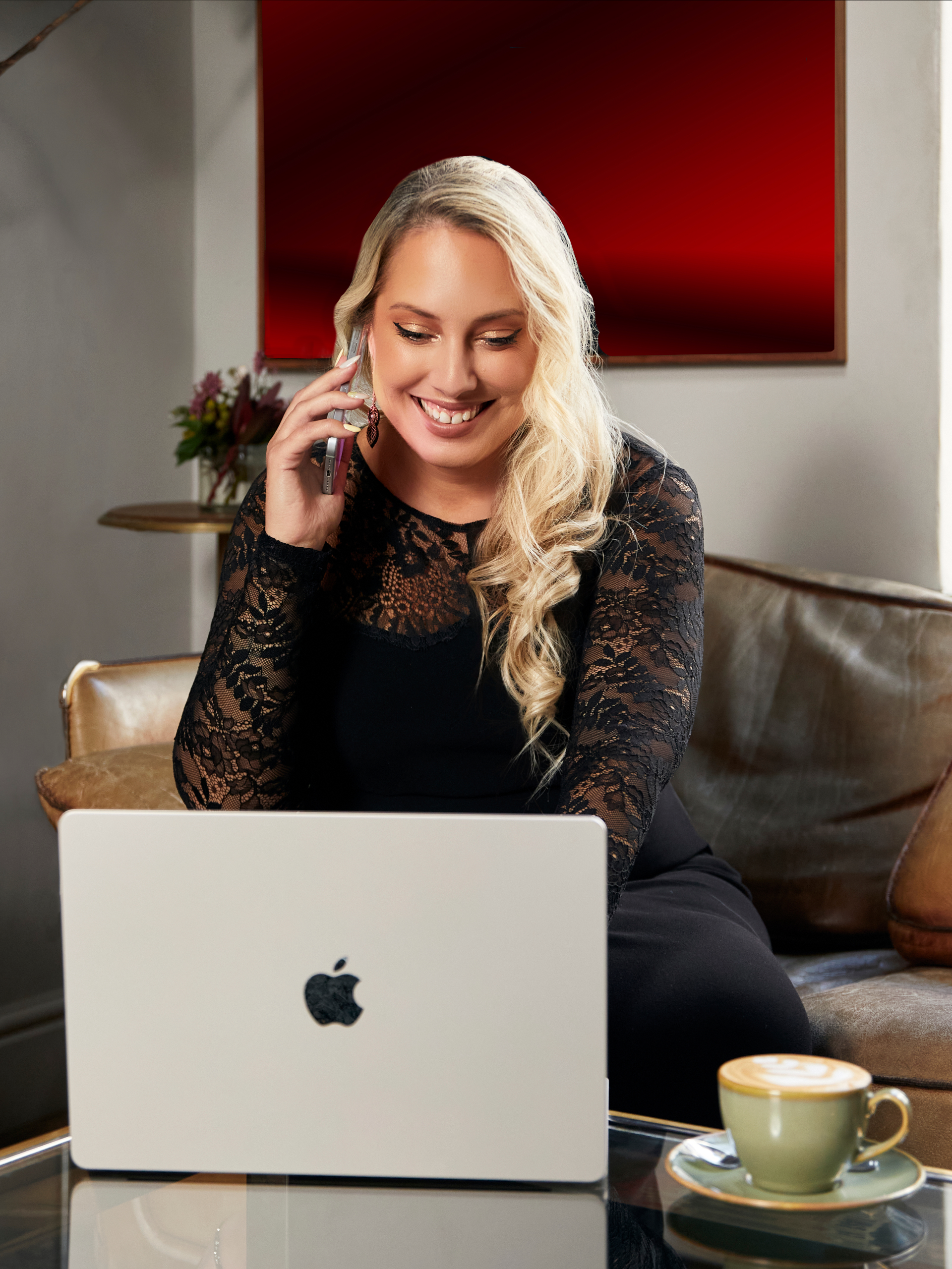Smiling woman on phone with laptop and notebook in cozy workspace.