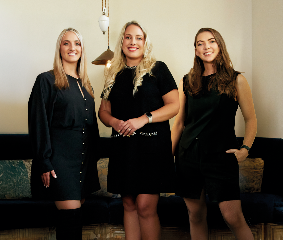Group of three women in black outfits posing together indoors.